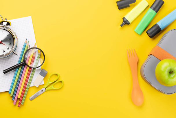 黄色の背景に学校用品、文房具、弁当箱。教育と栄養。余白のある平面 - 写真・画像