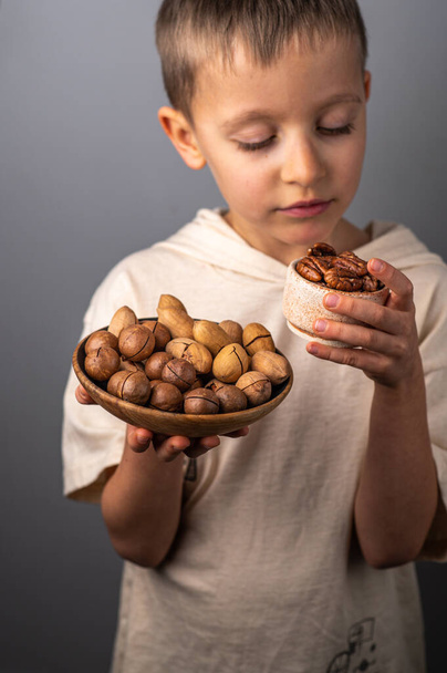 A little boy chooses between different nuts. Macadamia nuts and pecans. Healthy Eating. - Zdjęcie, obraz