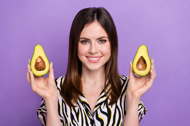 Portrait of cheerful nice girl beaming smile arms hold two halves avocado isolated on purple color background. - Φωτογραφία, εικόνα