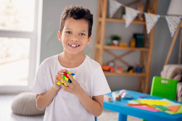 Photo of charming pretty small boy wear white t-shirt playing rubick cube indoors room home house. - Foto, immagini