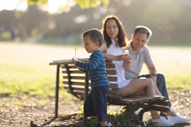 Rodzina w parku - uroczy chłopczyk dmuchający bańki mydlane. Środek strzału - Zdjęcie, obraz
