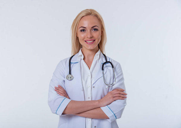 Ritratto di bella dottoressa in camice bianco che guarda la macchina fotografica e sorride in piedi con le braccia incrociate, isolata su sfondo bianco
 - Foto, immagini