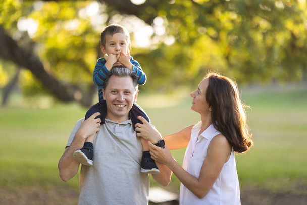 Carino famiglia bianca nel parco - piccolo figlio sulle spalle di suo padre. Mid shot - Foto, immagini