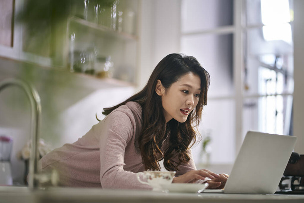 молода азіатська бізнес-леді фрілансерка, що працює на кухні вдома, використовуючи ноутбук
 - Фото, зображення