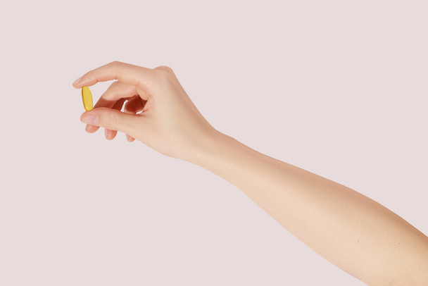 Mão segurando os suplementos (ômega 3, vitaminas) em fundo rosa - Foto, Imagem