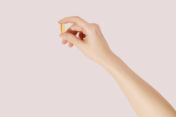 Рука держит добавки (омега 3, витамины) на розовом фоне - Фото, изображение