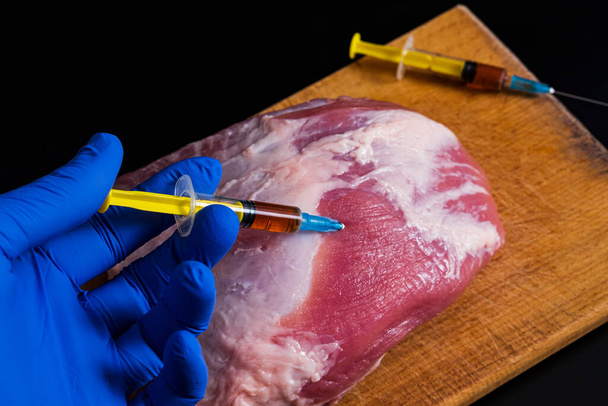 Injeção de uma seringa em carne crua em um fundo escuro.Ilustração conceitual de hormônios e antibióticos na produção de alimentos. - Foto, Imagem