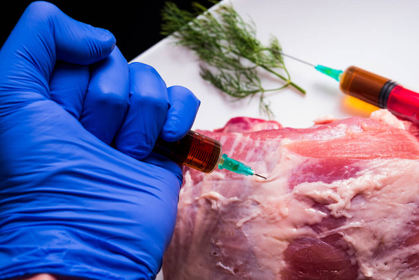 Inyección de una jeringa en carne cruda sobre un fondo oscuro.Ilustración conceptual de hormonas y antibióticos en la producción de alimentos. - Foto, imagen