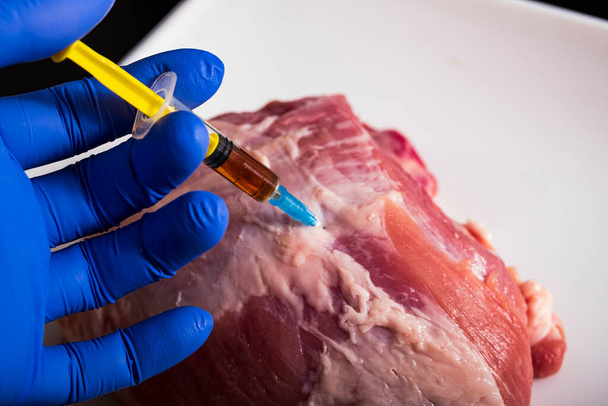 Ένεση από σύριγγα σε ωμό κρέας σε σκούρο φόντο.Έννοια απεικόνιση των ορμονών και των αντιβιοτικών στην παραγωγή τροφίμων. - Φωτογραφία, εικόνα