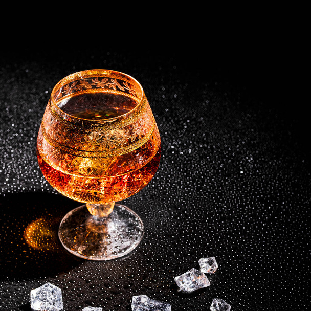 Glass with cognac and ice on a dark background. the concept of alcoholism and drinking - Foto, Imagem