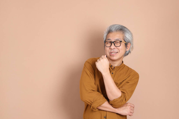 Los años 40 adulto asiático hombre con camisa amarilla de pie sobre el fondo marrón. - Foto, Imagen