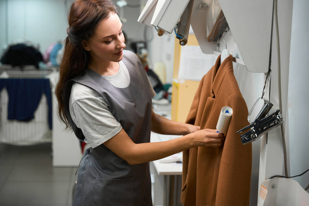 Woman laundry service worker cleaning coat with sticky lint remover, professional delicate fabrics cleaning - Foto, Imagem