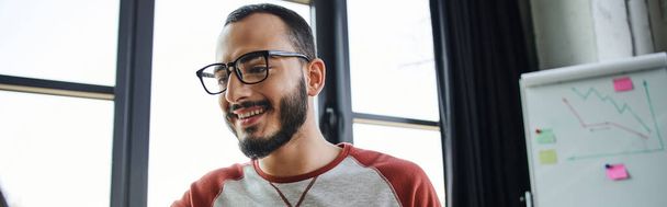 若い幸せな髭のマネージャーの肖像画近くの現代オフィスで働いている眼鏡背景、ビジネスライフスタイル、バナーに関するビジネス分析とフリップチャート - 写真・画像