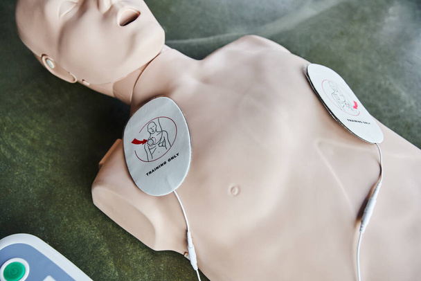 トレーニングルームの床に除細動器パッド付き心肺蘇生訓練用マネキンの高い角度ビュー、応急処置訓練やスキル開発のための医療機器 - 写真・画像