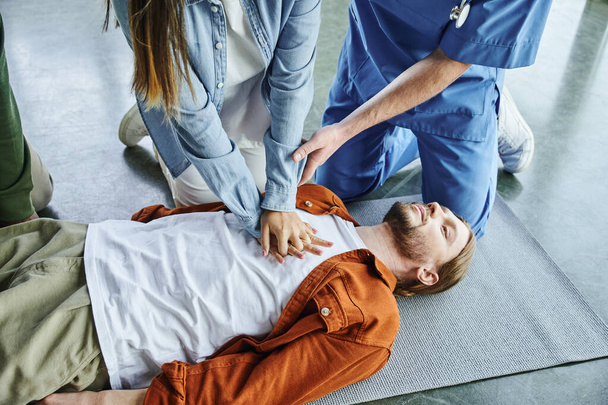 cardiopulmonary resuscitation, professional instructor helping woman practicing chest compressions on young man lying in training room, effective life-saving skills and techniques concept - Photo, Image