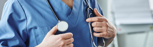 bijgesneden beeld van jonge gezondheidswerker in blauw uniform, met stethoscoop op de nek staande in de kliniek, EHBO-training seminar en nood paraatheid concept, banner - Foto, afbeelding