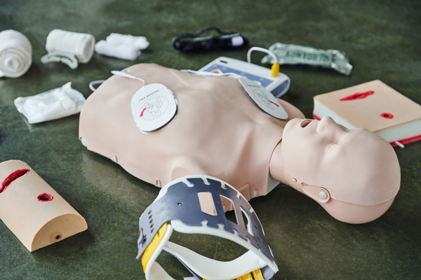 ανδρείκελο κατάρτισης CPR κοντά στον αυτόματο εξωτερικό απινιδωτή, προσομοιωτές περιποίησης τραυμάτων, στήριγμα λαιμού και επίδεσμοι δαπέδου σε αίθουσα εκπαίδευσης, ιατρικός εξοπλισμός για εκπαίδευση πρώτων βοηθειών και ανάπτυξη δεξιοτήτων - Φωτογραφία, εικόνα