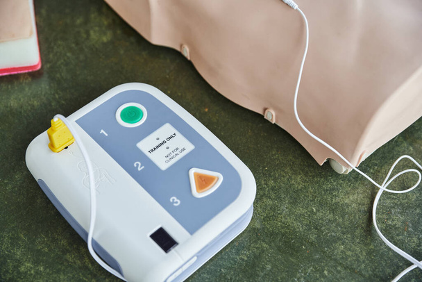vue grand angle du défibrillateur externe automatisé moderne près du mannequin CPR du plancher dans la salle d'entraînement, équipement médical pour la formation en premiers soins et le développement des compétences - Photo, image
