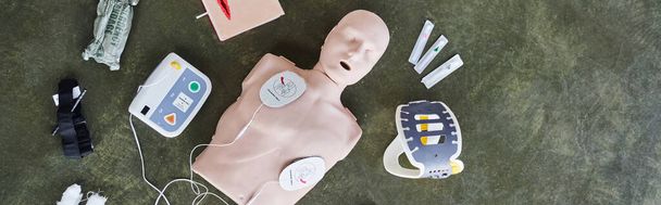 top view of automated external defibrillator, neck brace, syringes, compression tourniquet and bandages near CPR manikin, medical equipment for first aid training and skills development, banner - Photo, Image