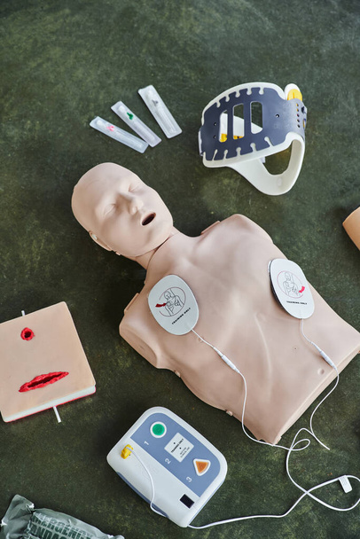 górny widok manekina resuscytacyjnego, zautomatyzowany defibrylator zewnętrzny, symulator pielęgnacji ran, stabilizator szyi i strzykawki, sprzęt medyczny do treningu pierwszej pomocy i rozwijania umiejętności - Zdjęcie, obraz