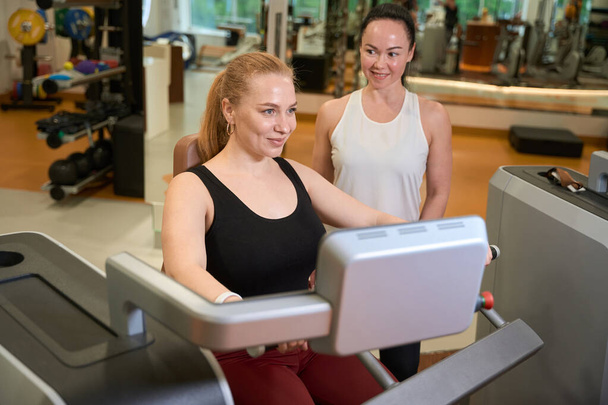 Two joyful female are in the gym of the fitness clinic, the blonde is engaged in the simulator - Fotoğraf, Görsel