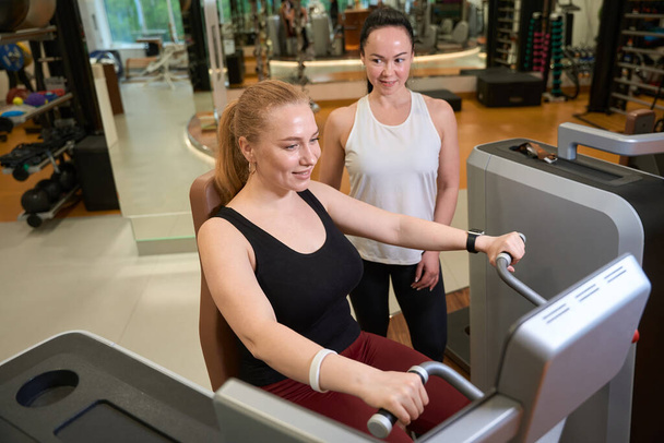 Two females are in the gym of the fitness clinic, the blonde is engaged in the simulator - Fotoğraf, Görsel
