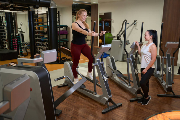İki kadın spor salonundalar, modern fitness ekipmanları etrafta. - Fotoğraf, Görsel
