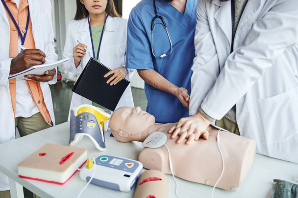 cropped view of african american man writing in notebook next to healthcare worker doing chest compressions on CPR manikin  during first aid seminar, life-saving skills hands-on learning concept - Photo, Image