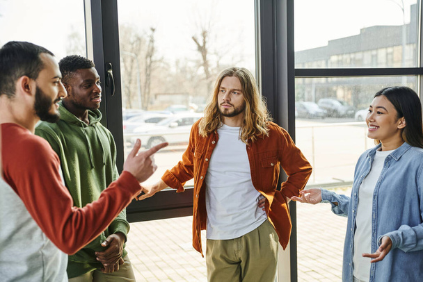 ambitious and stylish multiethnic colleagues gesturing and discussing startup project in modern office space, creative thinking, young and diverse business people collaboration - 写真・画像