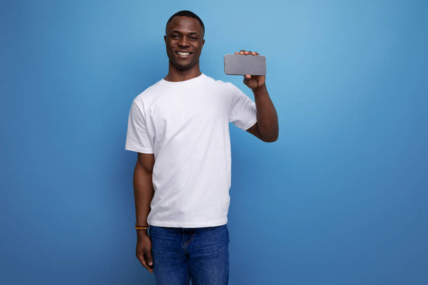 白いTシャツのハンサムなダークスキンの若いアメリカ人男性は携帯電話を示しています. - 写真・画像