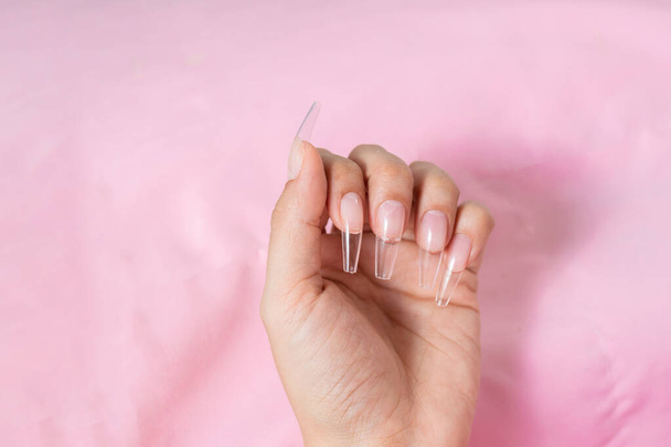 hand of a young woman on a pink background, with transparent false nails ready for a manicure - Fotografie, Obrázek