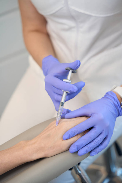 Detailní záběr kosmetolog ruce v rukavicích provádění injekce na zápěstí dospělé ženy v salonu krásy - Fotografie, Obrázek