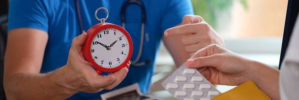 医者は目覚まし時計を持っていて薬を飲んでいる女性患者。薬を飲む時間 - 写真・画像