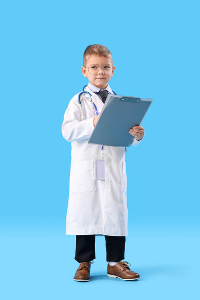 Cute little doctor with clipboard on blue background - Foto, Imagem