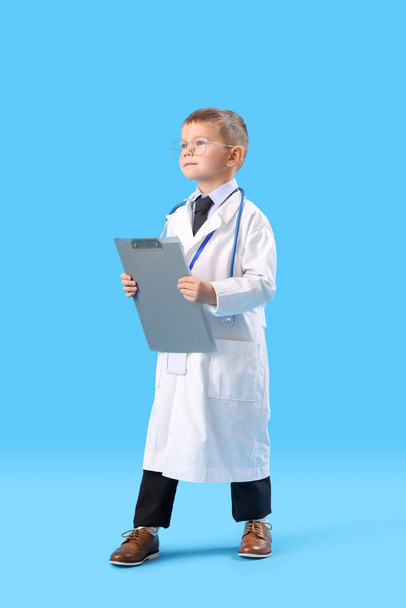 Cute little doctor with clipboard on blue background - Foto, immagini