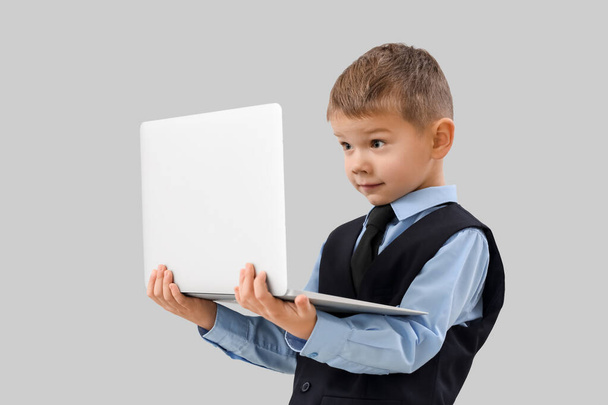 Lindo pequeño hombre de negocios con portátil sobre fondo gris - Foto, imagen