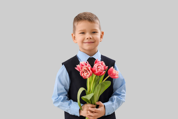 Cute little boy in suit with tulips on grey background - Photo, Image