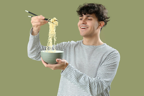 Young man eating tasty Chinese food on green background - Photo, Image