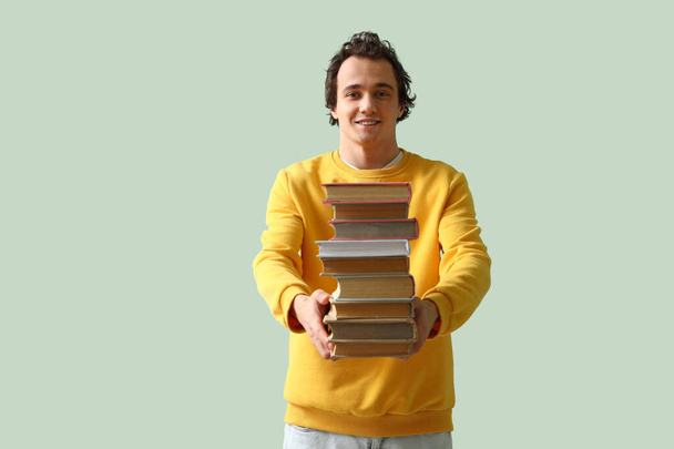 Junger Mann mit einem Stapel Bücher auf grünem Hintergrund - Foto, Bild