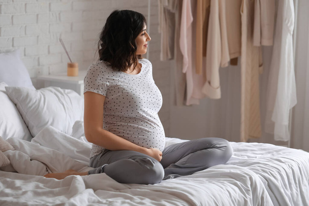 Nuori raskaana oleva nainen istuu makuuhuoneessa
 - Valokuva, kuva