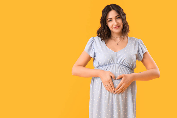 Young pregnant woman on yellow background - Фото, изображение