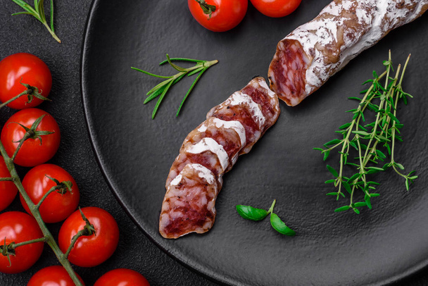Вкусная свежая копченая фуэ-колбаса с солью, специями и травами на темном бетонном фоне - Фото, изображение