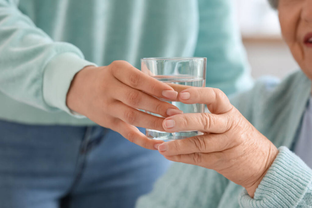 Young woman giving glass of water to her grandmother at home, closeup - Foto, afbeelding