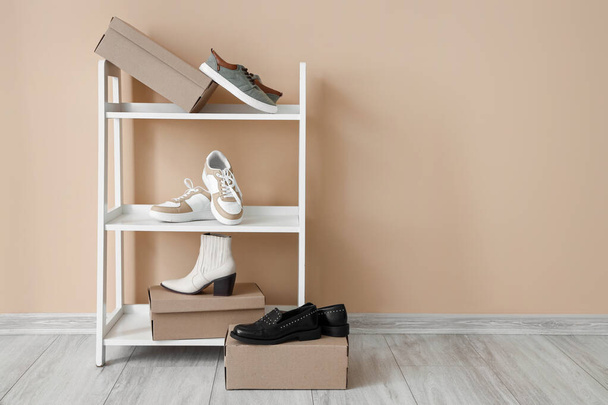 Shelving unit with cardboard boxes and different stylish shoes near color wall - Foto, Bild