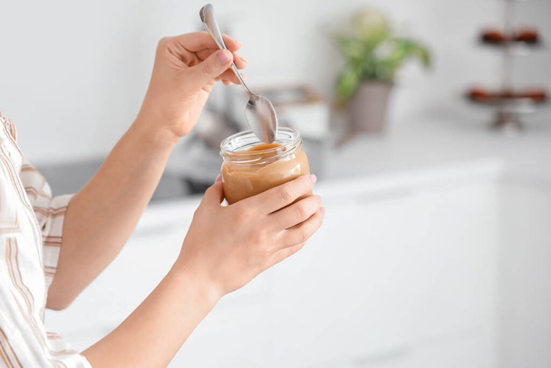 Mujer joven con cuchara y tarro de mantequilla de nuez en la cocina, primer plano - Foto, Imagen