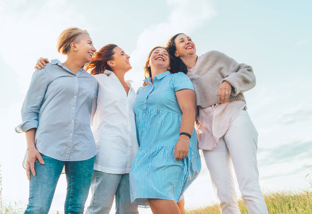 Portrait of four cheerful smiling and laughing women embracing during sunset time outdoors walking by the green hill. Woman's friendship, relations, and happiness concept image. - Foto, Imagen