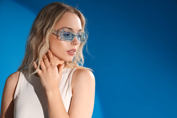 Young woman in stylish sunglasses on blue background, closeup - Zdjęcie, obraz