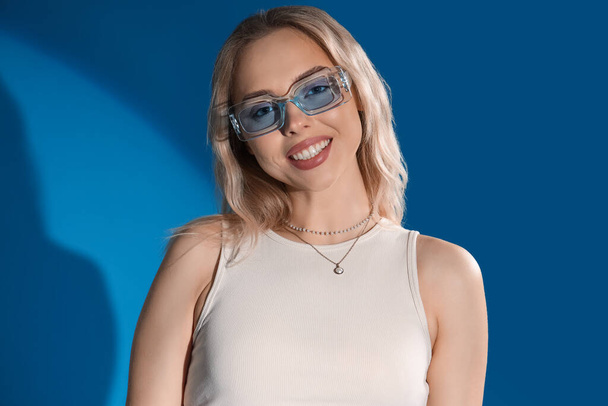Young woman in stylish sunglasses on blue background, closeup - Fotografie, Obrázek