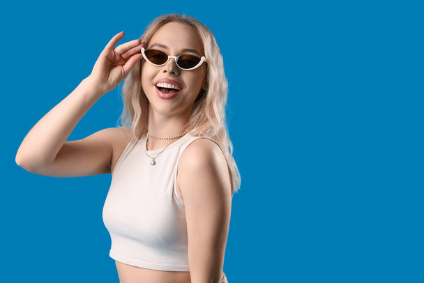 Fiatal nő stílusos napszemüveg kék háttér - Fotó, kép