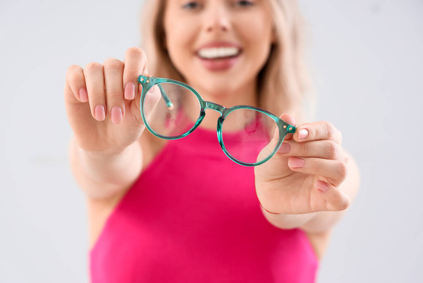 Mujer joven en gafas con estilo sobre fondo claro, primer plano - Foto, Imagen